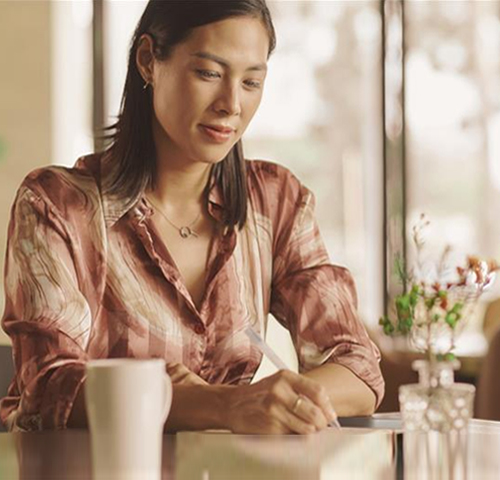 East Asian woman writing at the window